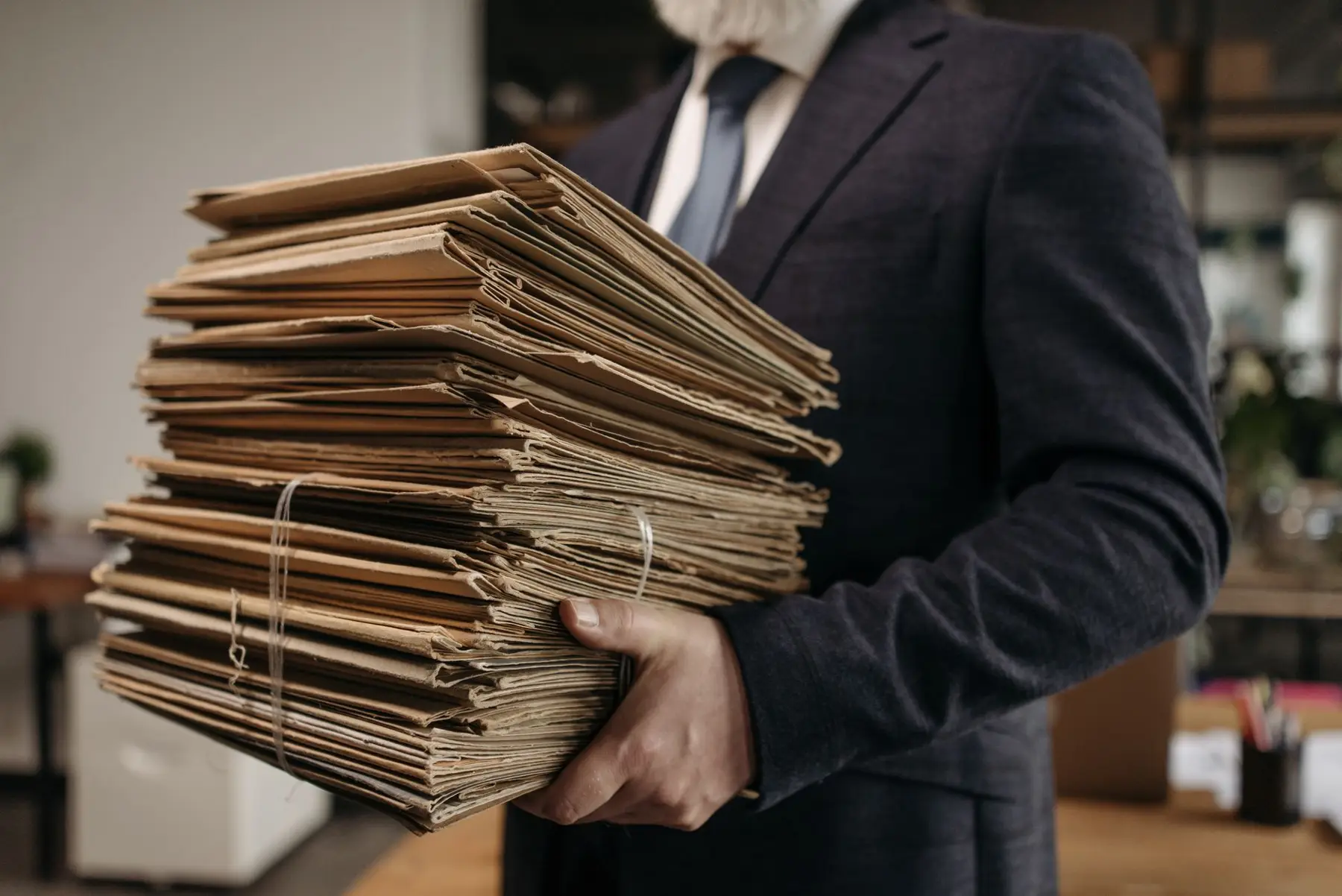 A man in a suit carrying a tall stack of old paper files